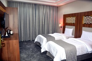 Hotellihuone, jossa on kaksi sänkyä, televisio, työpöytä ja suuri ikkuna, jossa on verhot.