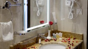 A bathroom with a marble sink, a mirror, a hairdryer, and a shower. - Salsbil Almasi (Madinah)