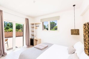 Ein Schlafzimmer mit einem Bett, einem Schreibtisch und einem Fenster mit Blick auf Grünflächen.