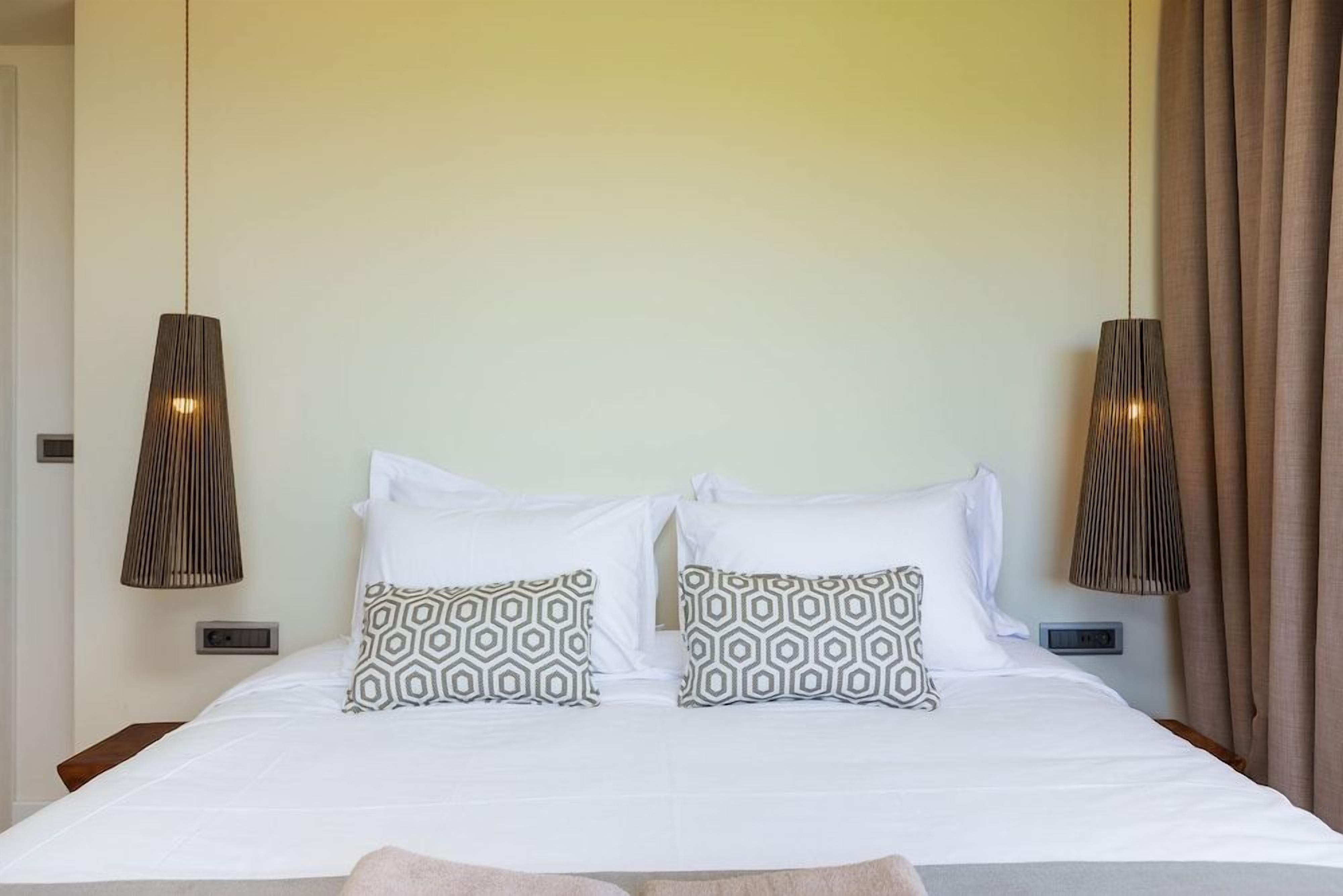 A hotel room with a bed, two bedside lamps, and a window with curtains.