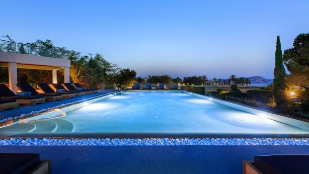 Piscina com espreguiçadeiras e pérgola, rodeada por um jardim ajardinado.