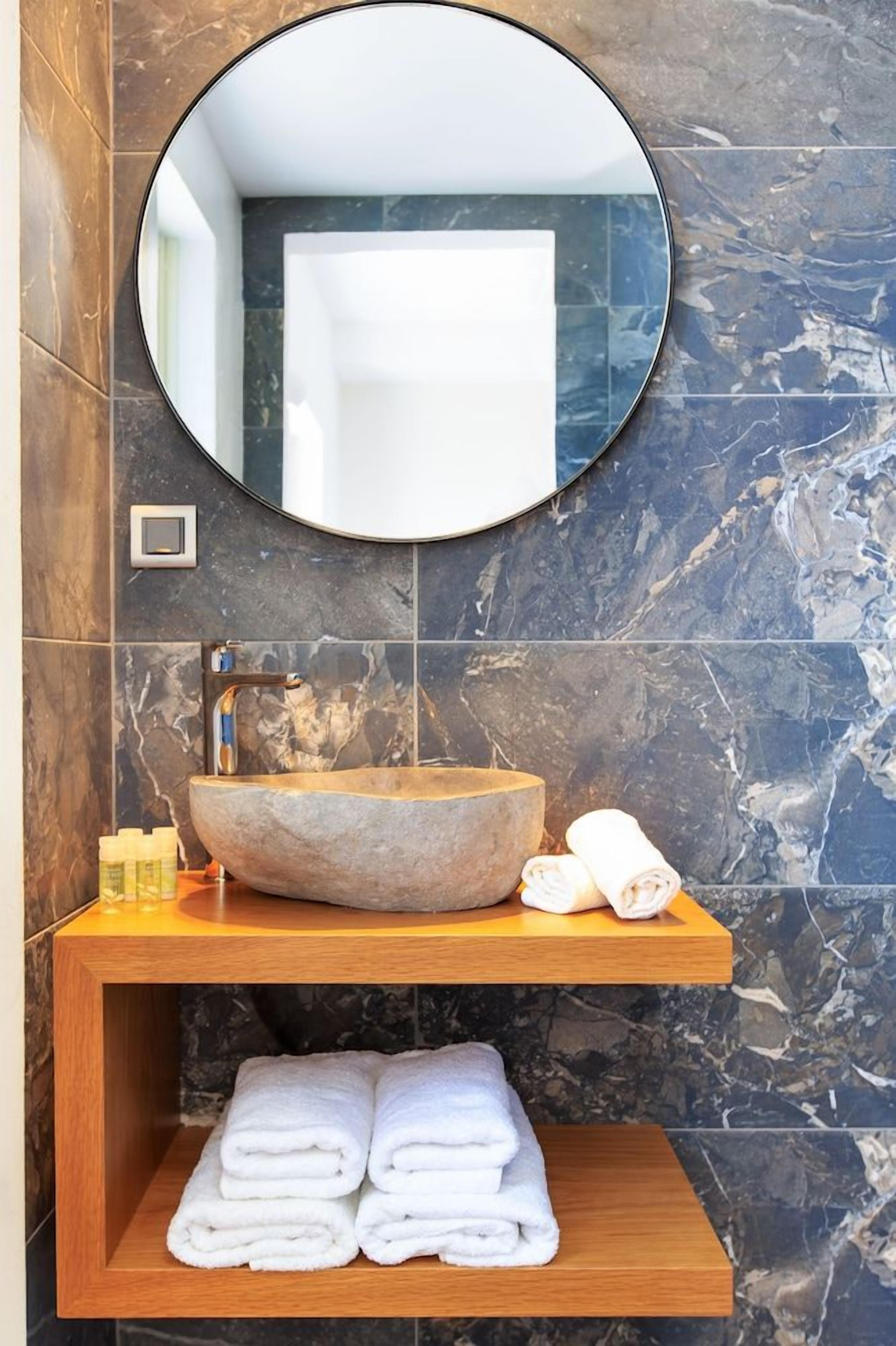 Un bagno con uno specchio rotondo, un lavandino in pietra e uno scaffale in legno con asciugamani.