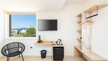 A modern room with a large window, a flat-screen TV, a small kitchen area with a coffee maker, and a black chair.