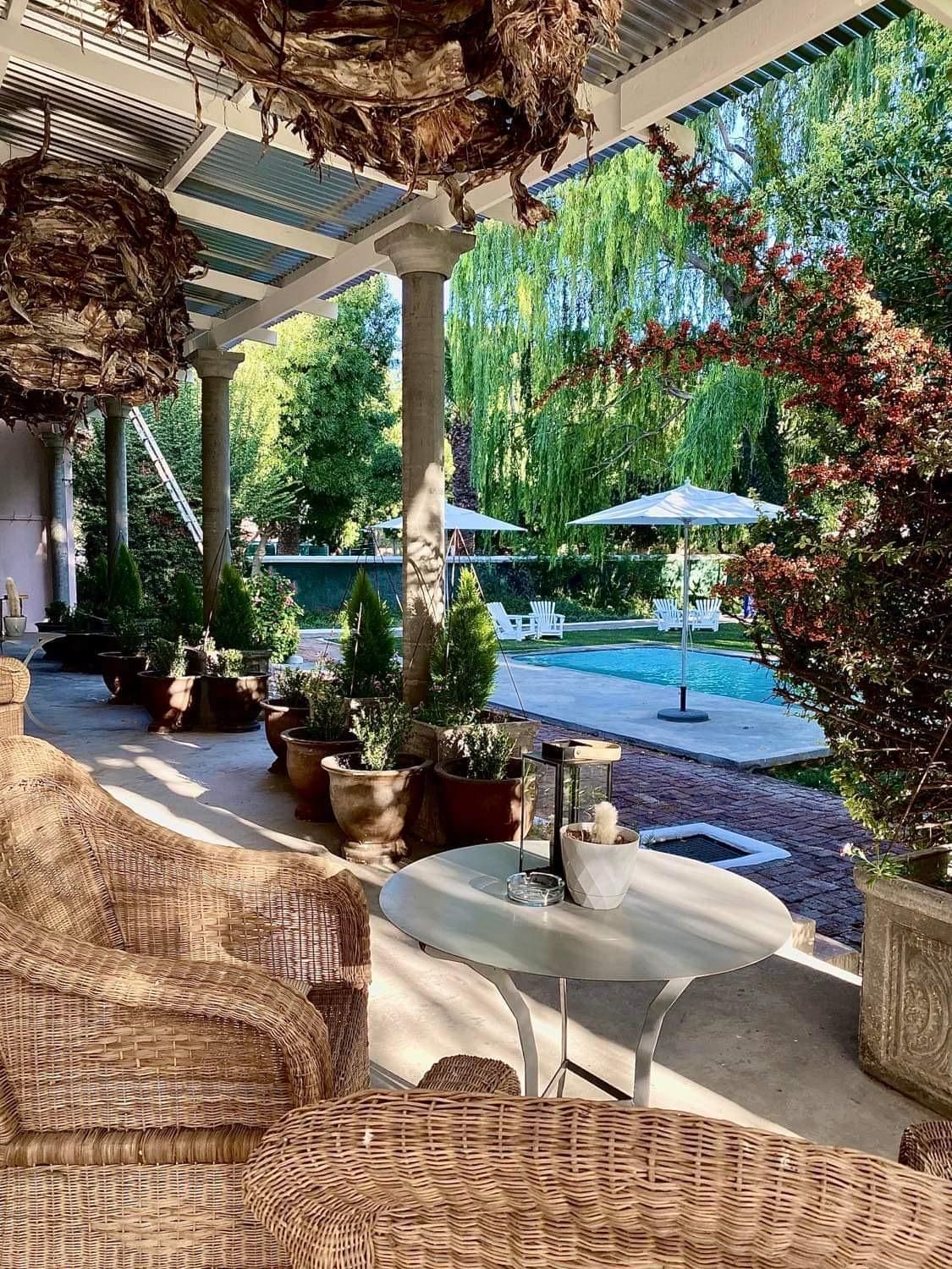 An outdoor patio area with wicker furniture, potted plants, and a view of a swimming pool.