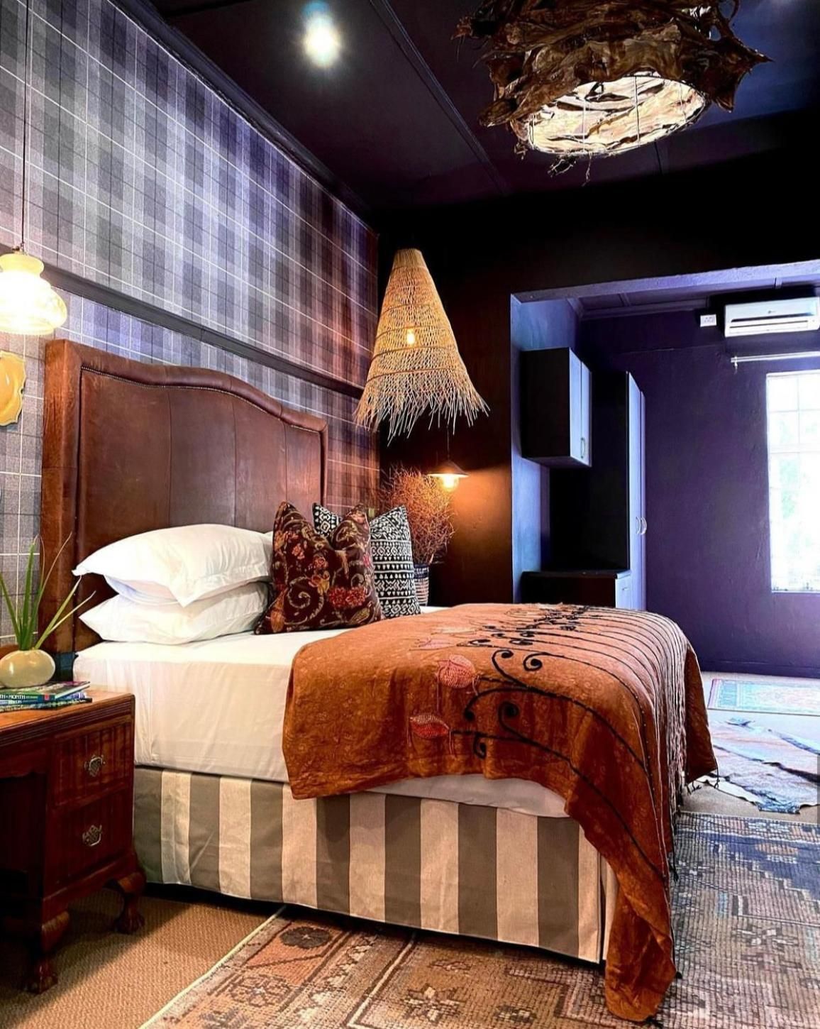 A bedroom with a large bed, a wooden headboard, a woven lamp, and a patterned rug.