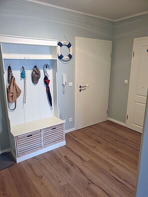 A room with a bench, a coat rack with bags and an umbrella, and a door with a life preserver hanging on it. - 1st floor, modern amenities, central location, about 200 m from the sandy beach (Baltic Sea) (Juliusruh)