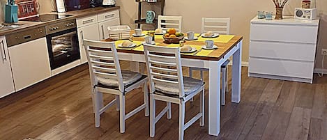 Una cocina moderna con armarios blancos, una mesa de comedor con sillas, un televisor en la pared y una mesa de centro de vidrio con un juego de mesa.