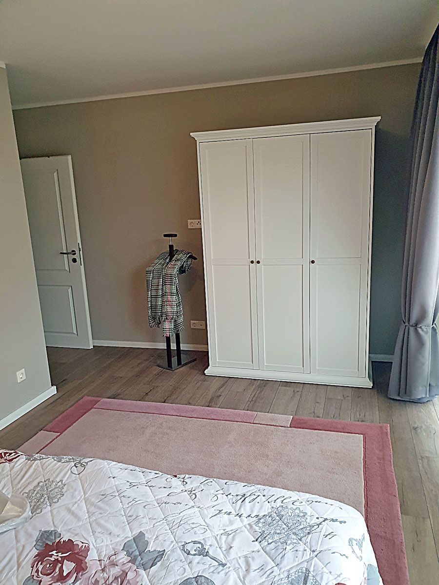 Un dormitorio con cama, armario, puerta y ventana con cortinas.