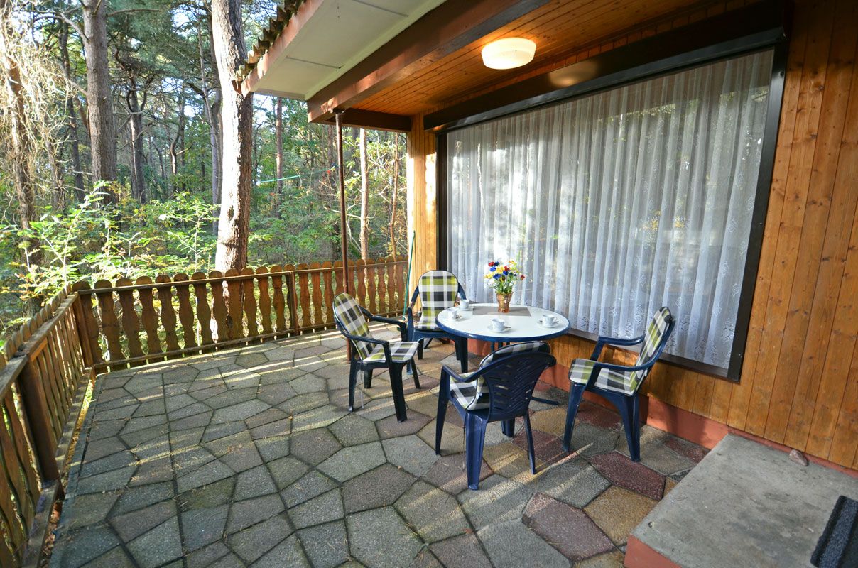 A covered patio with a table and chairs, surrounded by a wooden fence and a large window with curtains.