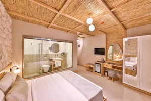 A modern bedroom with a large bed, a glass-enclosed shower, a vanity with a mirror, and a television. - Melisa Apart (Kaş)