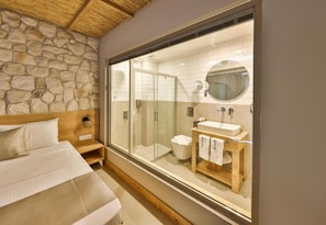 A bedroom with a large window, a stone wall, a wooden headboard, a bed, a nightstand, and a wooden cabinet with towels. - Melisa Apart (Kaş)