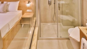 A modern bathroom with a glass-enclosed shower, a wooden bedside table, and a white sink. - Melisa Apart (Kaş)