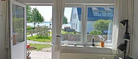A room with a bed, a window with curtains, a radiator, and a view of a building and greenery outside.