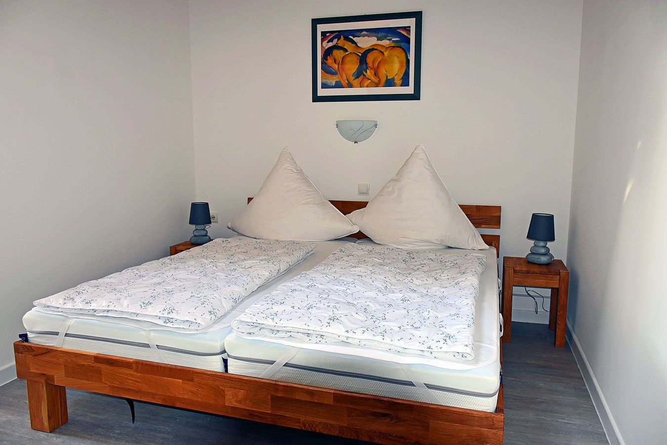 Una cama doble con estructura de madera, dos mesitas de noche con lámparas, una obra de arte colgada en la pared y un adorno decorativo en la pared.