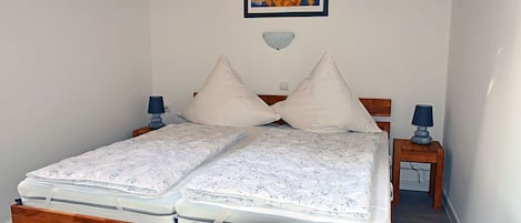 Una cama doble con estructura de madera, dos mesitas de noche con lámparas, una obra de arte colgada en la pared y un adorno decorativo en la pared.