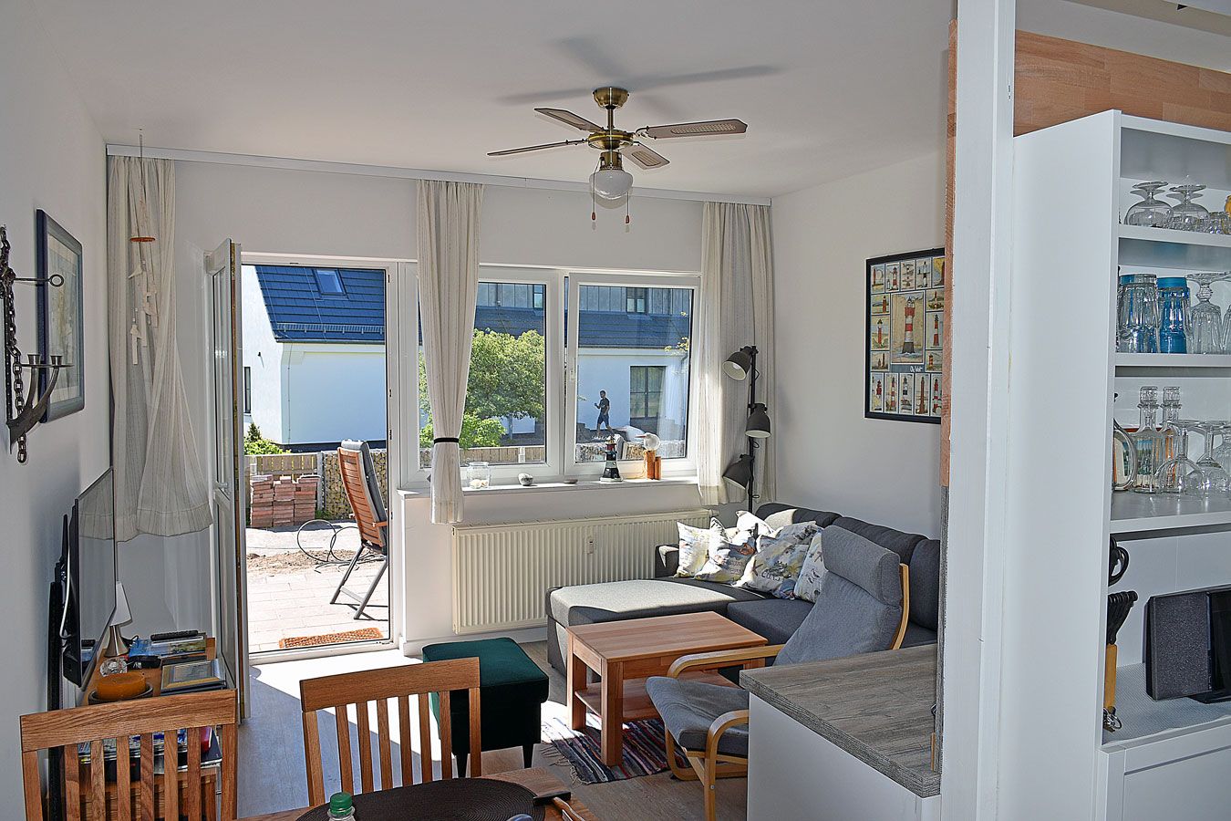 Ein Zimmer mit einer Couch, einem Tisch, einem Stuhl, einem Deckenventilator und Blick ins Freie.