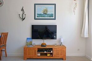 A living room with a wooden TV stand, a framed picture of a ship, and a wall-mounted light fixture. - Modern vacation rental with ocean views, just 60 meters from the water, 2 bedrooms, Wi-Fi, pets allowed (Dranske)