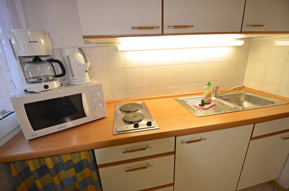 Una cucina compatta con forno a microonde, macchina del caffè e lavello.