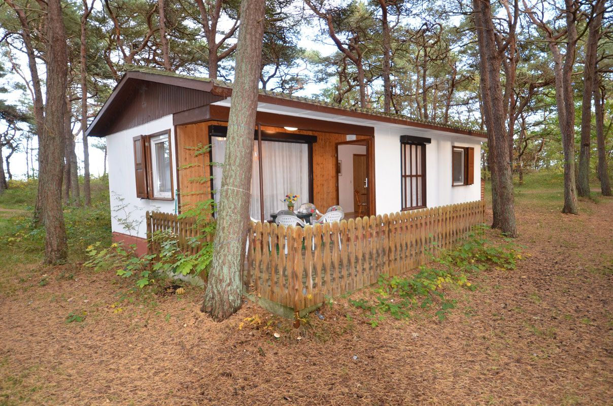 A small cabin with a wooden deck, surrounded by trees.