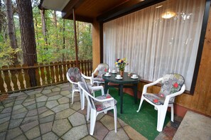 A covered outdoor seating area with a table set for two, surrounded by chairs, a wooden fence, and a view of a forested area. - Bungalow right on the sandy beach of the Baltic Sea, sleeps up to 4 people with 2 bedrooms (Juliusruh)