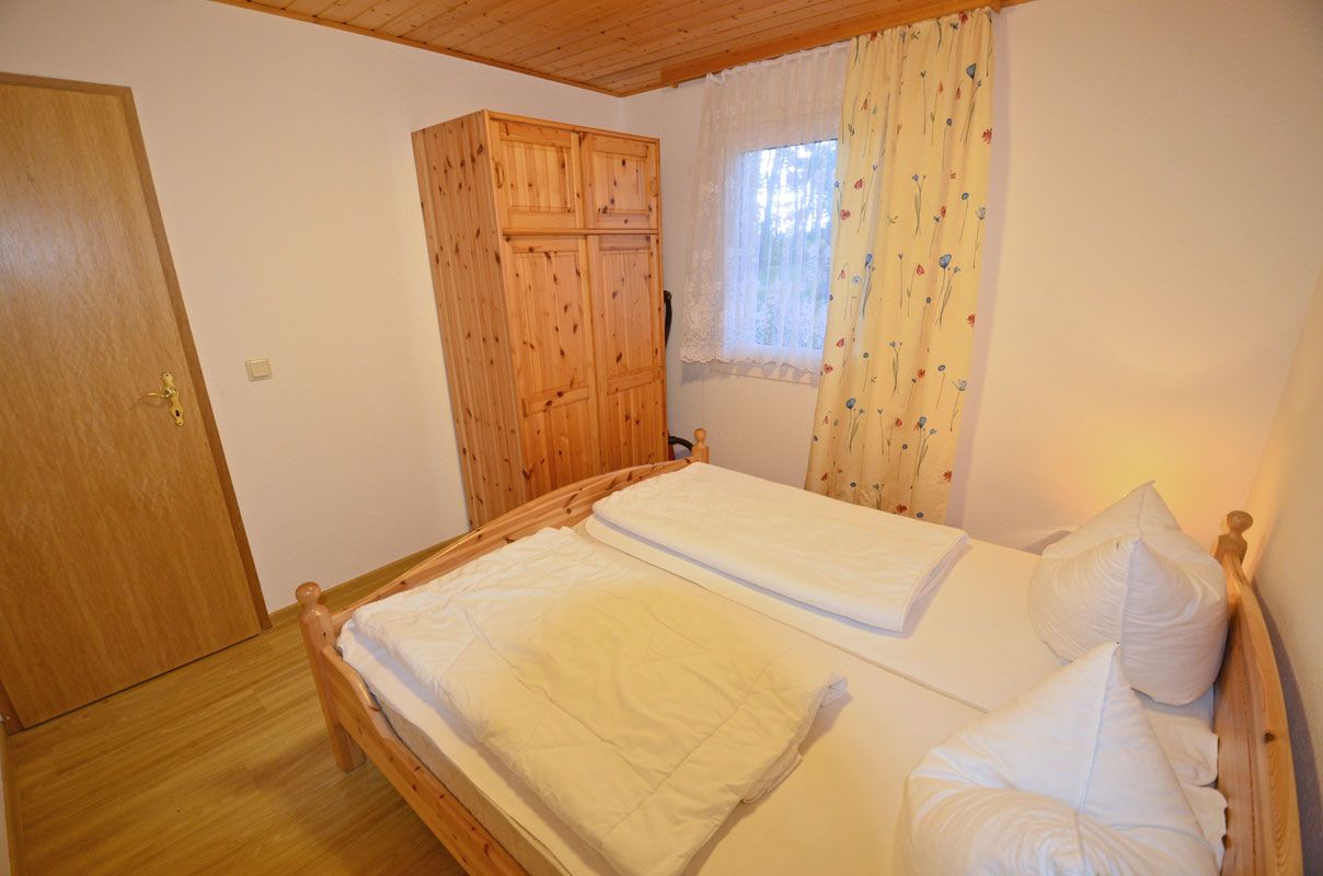 Une chambre avec un lit en bois, une armoire et une fenêtre ornée de rideaux à motifs floraux.