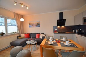 Uma sala de estar moderna com sofá, mesa de jantar para dois e cozinha equipada com fogão e micro-ondas.