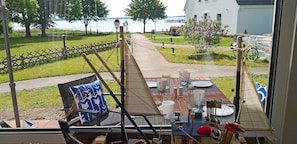 A dining area with a table set for two, overlooking a grassy area and a body of water. - Vacation rental with a view of the water, 2 bedrooms, just 60 meters from the water, Wi-Fi (Dranske)