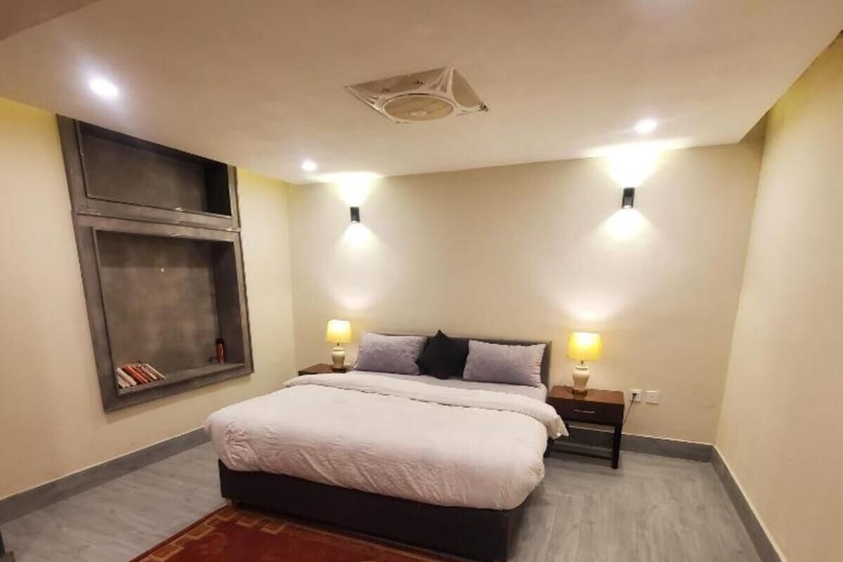 A bedroom with a bed, two bedside lamps, a wall-mounted shelf, and a red rug.