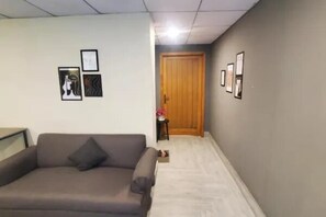Ein Zimmer mit einem grauen Sofa, einer Holztür und gerahmten Bildern an den Wänden.
