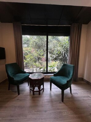 A room with two green armchairs, a small round table, and a large window with curtains. - Garden Hotel (Islamabad)