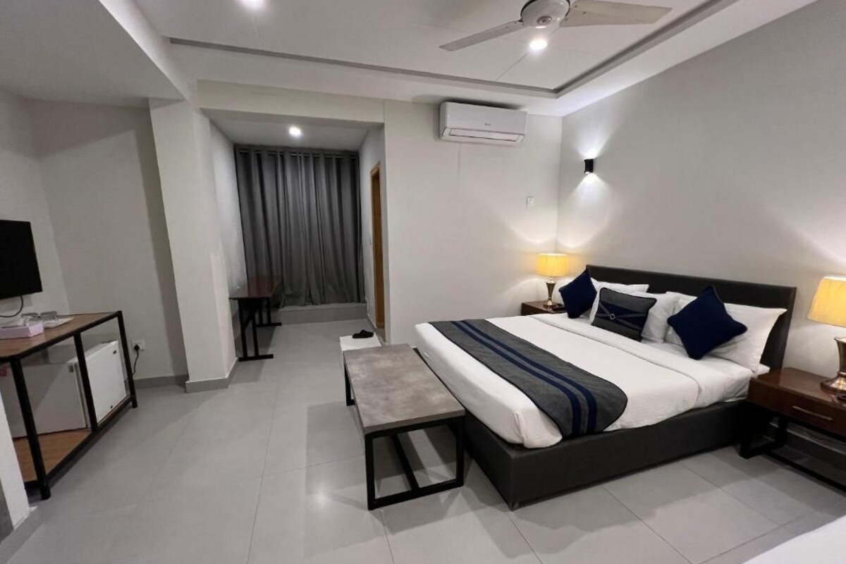 A modern hotel room with a large bed, bedside lamps, a desk, and a small seating area.