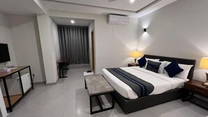 Quarto de hotel moderno com uma cama grande, abajures, uma escrivaninha e um pequeno espaço de estar.
