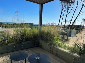 A covered outdoor seating area with two tables, overlooking a landscaped garden and a view of the beach. - Casa Grande Hotel & Beach Club (José Ignacio)