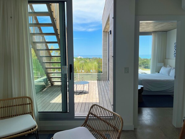 A room with a bed, a wicker chair, and a view of the ocean through a sliding door. - Casa Grande Hotel & Beach Club (José Ignacio)