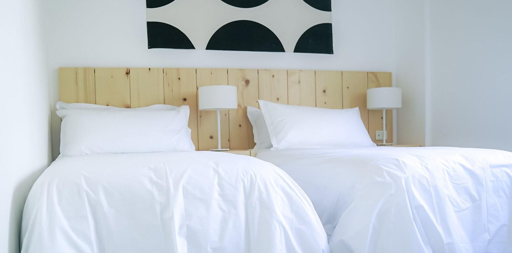 Een tweepersoonsbed met witte lakens, twee nachtkastjes met lampen en een houten hoofdbord.