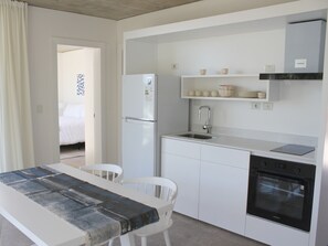 A compact kitchen with a refrigerator, sink, oven, and a dining area with a table and chairs. - Casa Grande Hotel & Beach Club (José Ignacio)