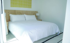 A neatly made bed with white linens in a room with a wooden headboard and a small bedside table with a lamp. - Casa Grande Hotel & Beach Club (José Ignacio)