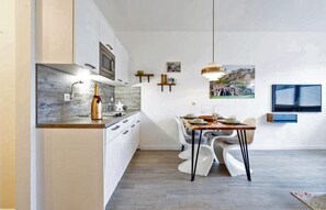 Eine moderne Küche mit weißen Schränken, einer Marmorarbeitsplatte und einem Essbereich mit weißen Stühlen und einem Holztisch.
