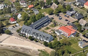 Eine Vogelperspektive zeigt eine Wohngegend mit einem großen Gebäude mit grauem Dach, einem Parkplatz und einem Strand im Vordergrund.