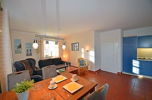 Ein modernes Wohnzimmer mit einer Couch, Esstisch, Stühlen und einer Küchenzeile mit Schränken.