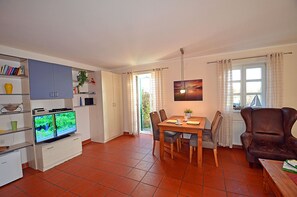Ein Wohnzimmer mit Fernseher, Esstisch, Stühlen, einer Couch und einem Bücherregal.