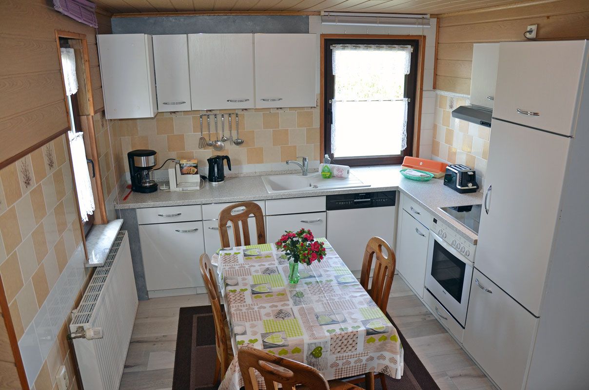 Een kleine keuken met een eettafel, stoelen, een koffiezetapparaat, een broodrooster en een koelkast.