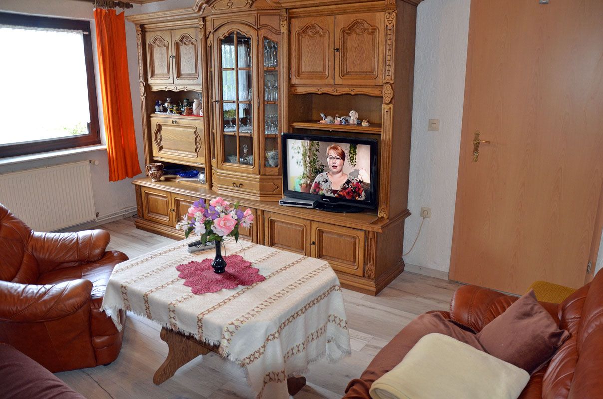 A living room with a wooden cabinet, a television, a table with a vase of flowers, and leather sofas.