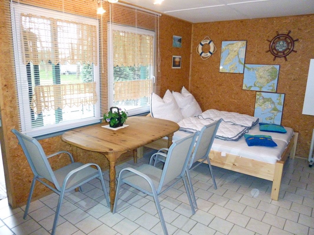 A room with a wooden table, chairs, a bed, and a window with blinds.