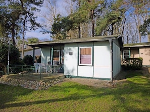 A small, single-story building with a covered patio area, a stone pathway leading to the entrance, and a grassy lawn. - Bungalow right on the sandy beach of the Baltic Sea, sleeps up to 2 people, with 1 bedroom (Juliusruh)