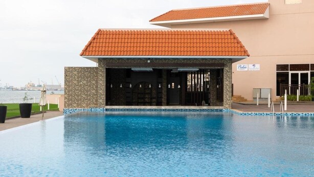 Uma piscina com área coberta, vista para o mar e um edifício com telhado em azulejos.