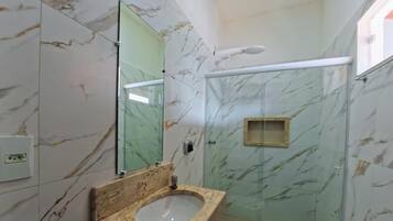 Um banheiro com parede de mármore, box de vidro, pia com bancada de mármore e vaso sanitário.