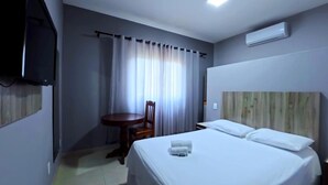 A hotel room with a bed, a desk, a chair, a television, and an air conditioning unit. - Plaza Hotel (Sinop)