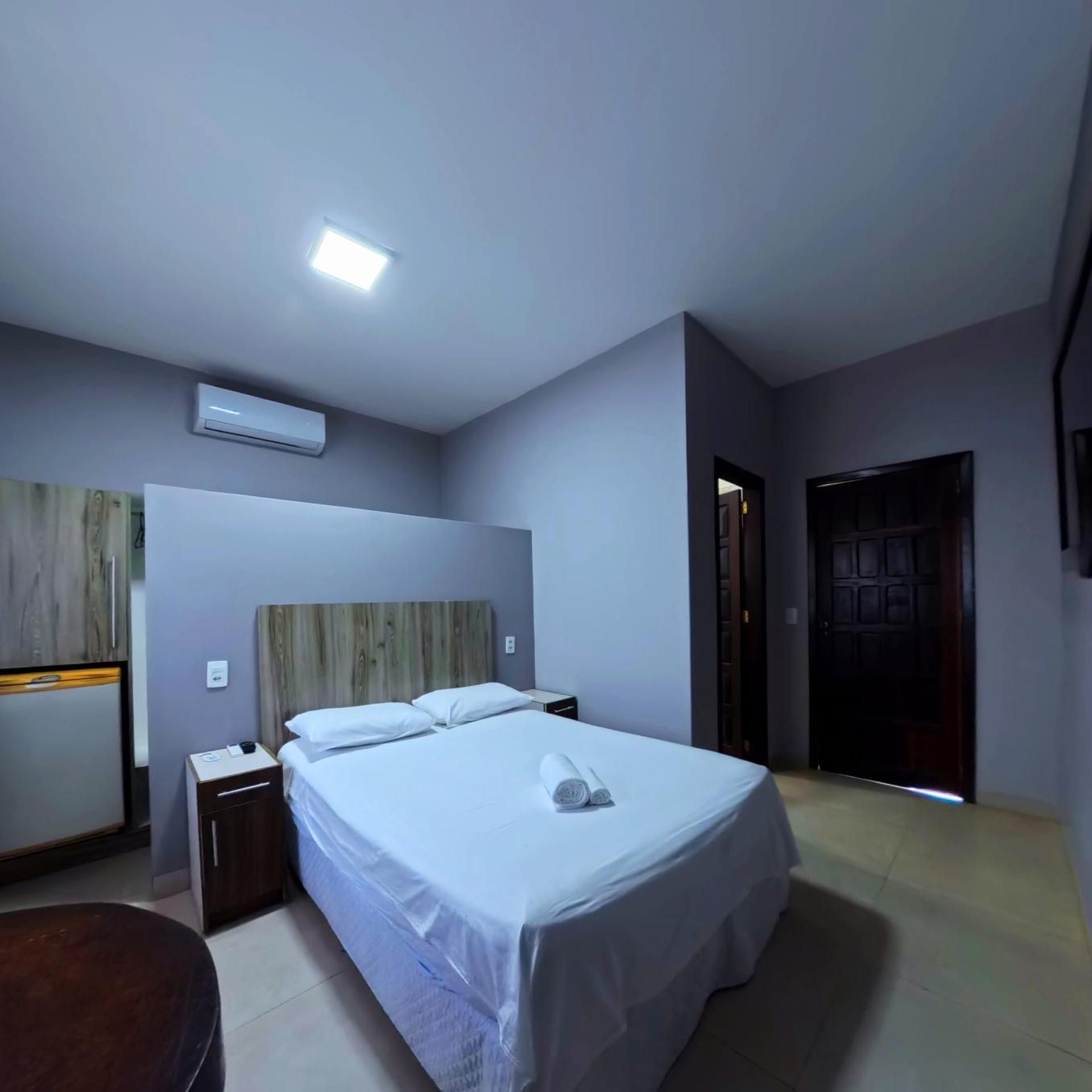 Quarto de hotel com cama, mesas de cabeceira, ar condicionado e porta.