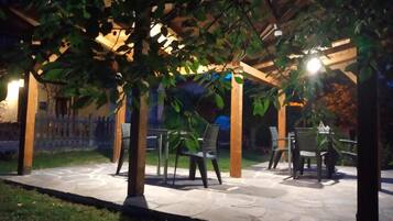 En utomhusplats med stengolv, en träpergola och metallstolar.